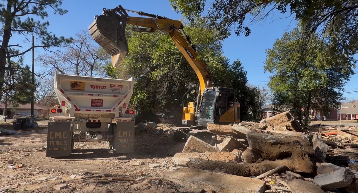 Excavator loading concrete debris into dump trailer